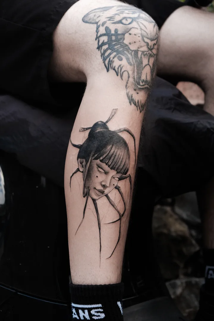 A girl's head with a bun and bangs, eyes closed, set on long spider legs, black and grey on the calf